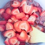 Sliced strawberries in a mixing bowl with a wooden spatula, prepared for cooking or baking.