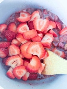 Sliced strawberries in a mixing bowl with a wooden spatula, prepared for cooking or baking.