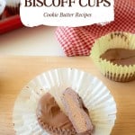 A chocolate-covered Biscoff Cups cookie butter treat sits in a cupcake liner, one half cut open to reveal its creamy filling, with more Biscoff Cups and a red checkered cloth in the background.