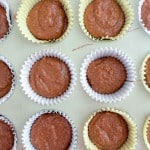 Unbaked chocolate cupcake batter in paper liners arranged in rows on a light-colored surface.