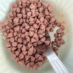 A metal spoon rests in a bowl filled with milk chocolate chips.