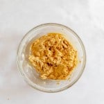 A clear glass bowl filled with mixed cookie dough sits on a white surface.