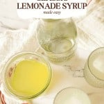Top-down view of a jar, glasses, and a bowl of Classic Lemonade Syrup on a white cloth, with text reading "Classic Lemonade Syrup made easy.