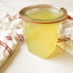 A glass jar with a sealed lid containing classic lemonade syrup sits on a white surface next to a white towel with red stripes.