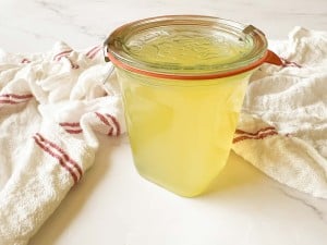 A glass jar with a sealed lid containing classic lemonade syrup sits on a white surface next to a white towel with red stripes.
