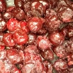 Close-up of cooked or stewed whole cherries with a glossy, deep red appearance and textured surface.