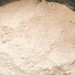 Close-up view of a pile of light brown flour or powder with a fine, slightly clumpy texture.