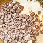 A pile of chocolate chips on top of a mixture of melted butter, sugar, and flour in a mixing bowl.
