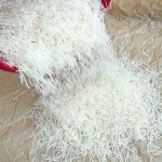 Thin white vermicelli noodles are being poured from a red container onto a sheet of brown parchment paper.
