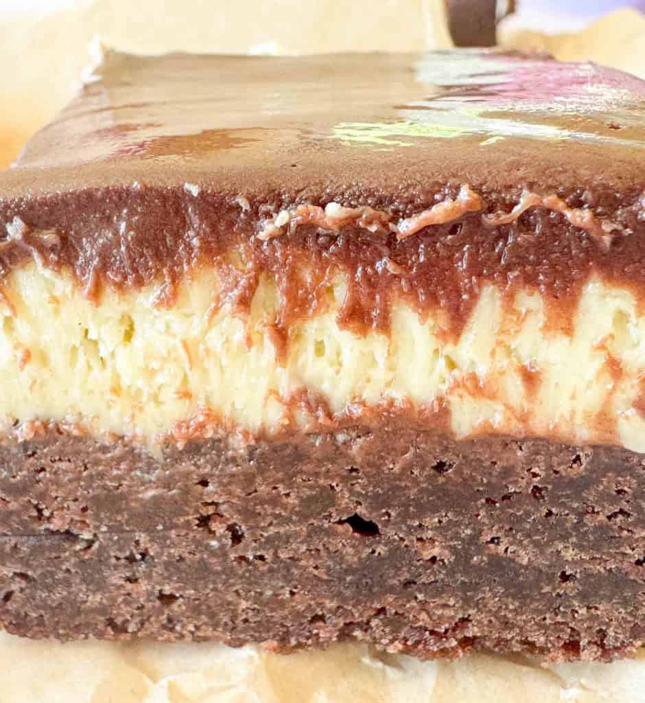 Close-up of a layered dessert with a dense chocolate base, creamy cheesecake middle, and smooth chocolate topping.
