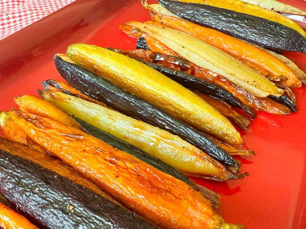 Rows of roasted rainbow carrots, including orange, yellow, and purple varieties, arranged on a red serving platter.