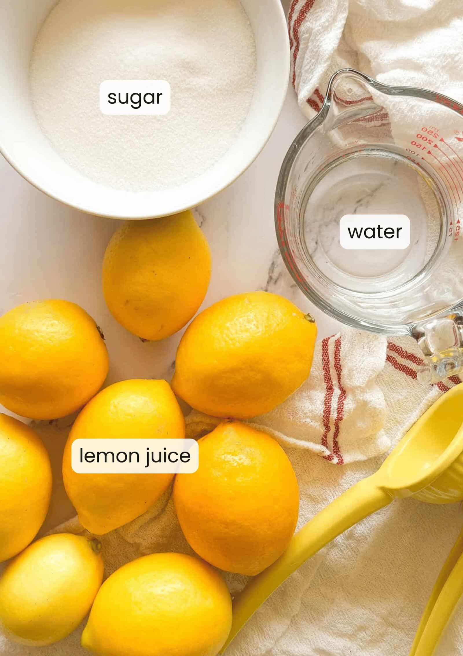 Bowl of sugar, measuring cup of water, whole lemons, and a lemon squeezer on a cloth; labels indicate sugar, water, and Classic Lemonade Syrup.