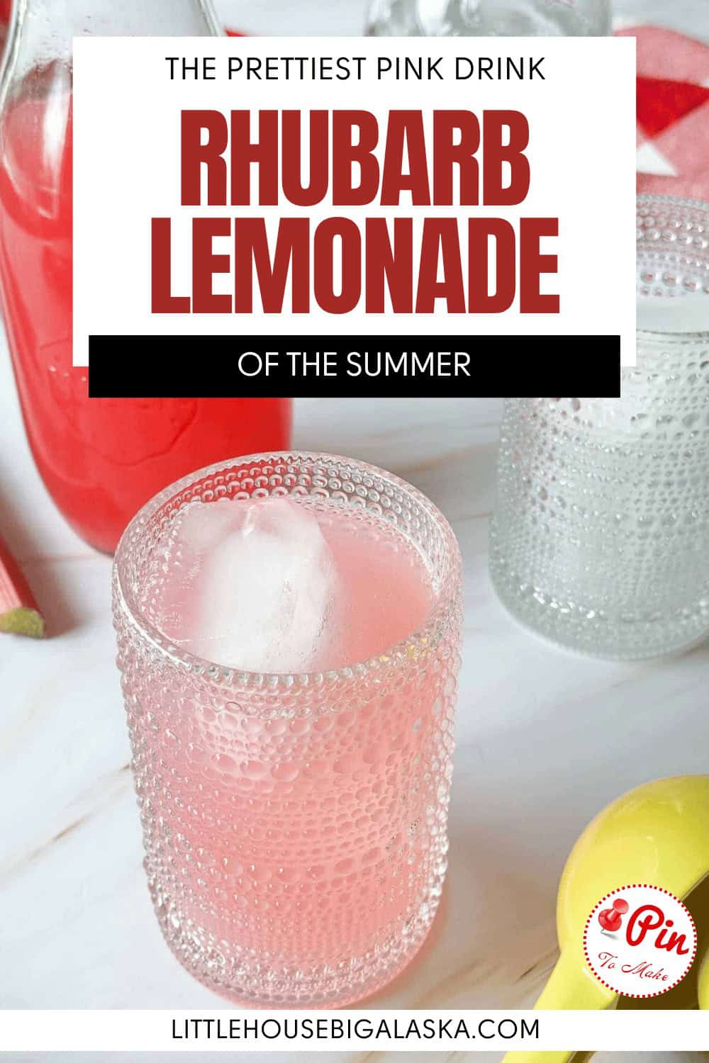 A glass of rhubarb lemonade with ice sits on a white surface next to another glass, a lemon, and a bottle of the same refreshing rhubarb lemonade.