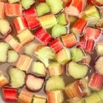 Chopped pieces of rhubarb in shades of red and green soak in water, perfect for making refreshing rhubarb lemonade.