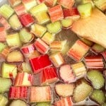 Chopped rhubarb pieces simmering in liquid, being stirred with a wooden spoon—perfect for making refreshing rhubarb lemonade.