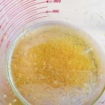 Close-up of grated lemon zest and juice in a clear glass measuring cup with red measurement markings.
