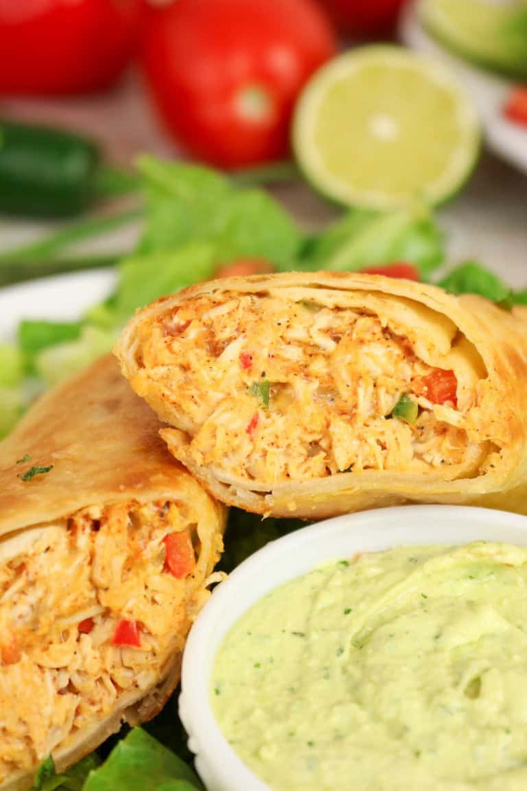 A close-up of a halved Firecracker Chicken Wraps burrito with shredded filling, served on lettuce with a side of creamy green dip.