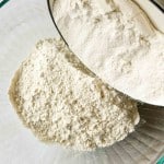 Flour being poured from a metal container into a clear glass bowl.