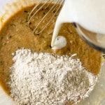Flour and milk being added to a brown batter in a mixing bowl with a whisk.