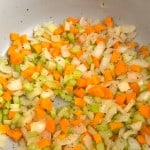 Chopped onions, carrots, and celery sautéing in a pan with herbs form the flavorful base for an easy chicken noodle soup.