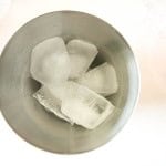 Stainless steel cup containing several large ice cubes, viewed from above on a white surface.