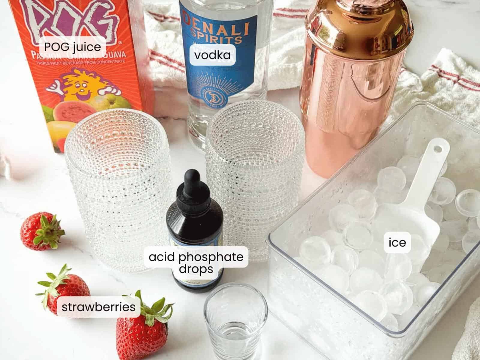 Ingredients for an Island Screwdriver cocktail are arranged on a counter: POG juice, vodka, acid phosphate drops, strawberries, textured glasses, a cocktail shaker, and a container of ice with a scoop.
