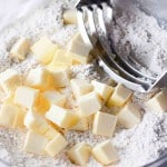 Cubes of butter and flour are being mixed with a pastry cutter in a glass bowl, forming the perfect base for delicious pumpkin buttermilk biscuits.