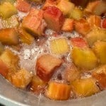 Chopped rhubarb pieces simmering in a pot with bubbling liquid, stirred with a wooden spoon.