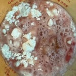 A glass measuring cup with a frothy pink liquid and lumps of white powder on the surface.