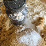 Close-up of a food processor bowl with flour, brown sugar, and baking powder inside, before mixing.