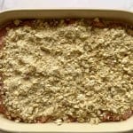 A rectangular baking dish filled with an unbaked oat crumble topping over sliced fruit, ready to be baked.