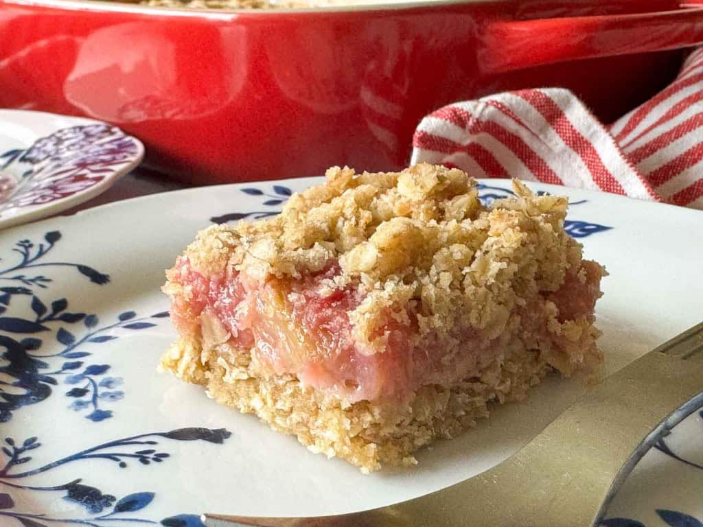 A square piece of fruit crumble bar with a golden oat topping sits on a white plate with blue floral patterns.