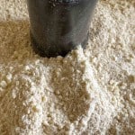 A black container sits partially buried in a pile of finely ground, off-white powder with small granules.