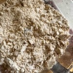 A close-up of a glass mixing bowl containing a dry, crumbly mixture of flour and oats, likely in the early stages of baking preparation.