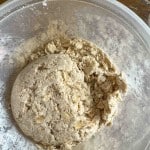 A clear bowl containing partially mixed dough with visible oats and flour on the sides.
