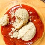 A glass bowl containing ketchup and packed brown sugar on a wooden surface.