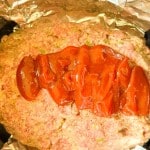 Raw meatloaf mixture in a foil-lined pan topped with a layer of tomato sauce or ketchup.