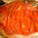 A meatloaf covered with a layer of red sauce sits on aluminum foil.