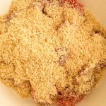 A close-up of uncooked ground meat covered with a layer of breadcrumbs in a white mixing bowl.
