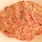 A close-up of a mound of raw ground meat mixed with herbs and spices in a bowl.