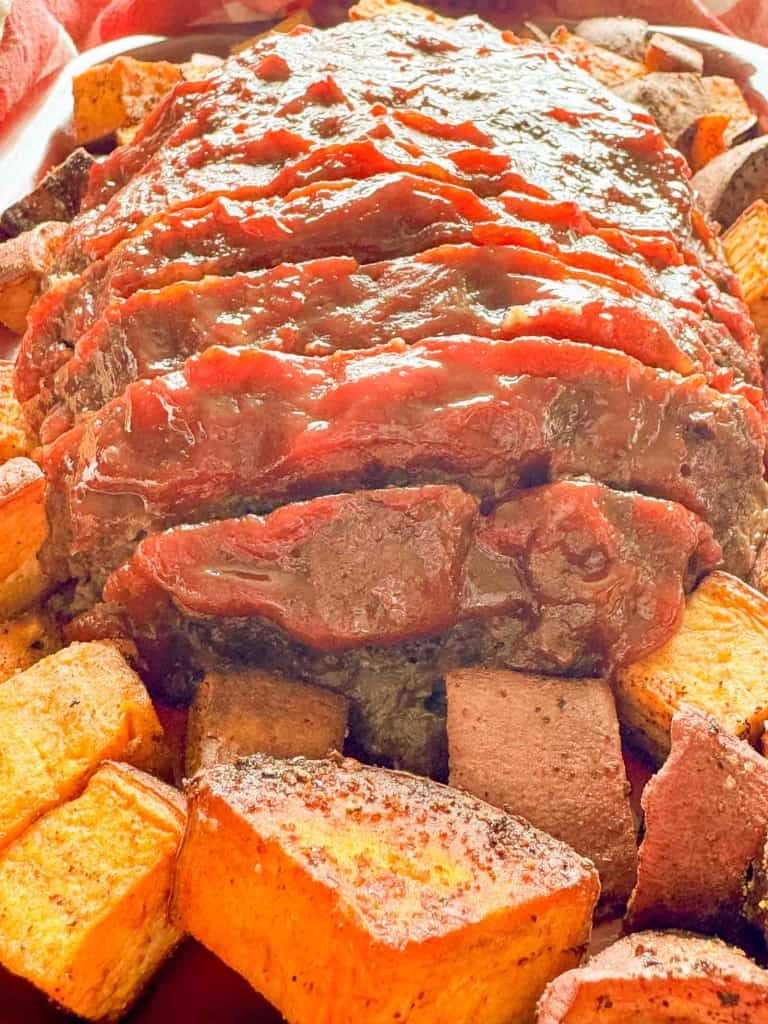 A glazed meatloaf is surrounded by roasted sweet potato cubes on a platter.