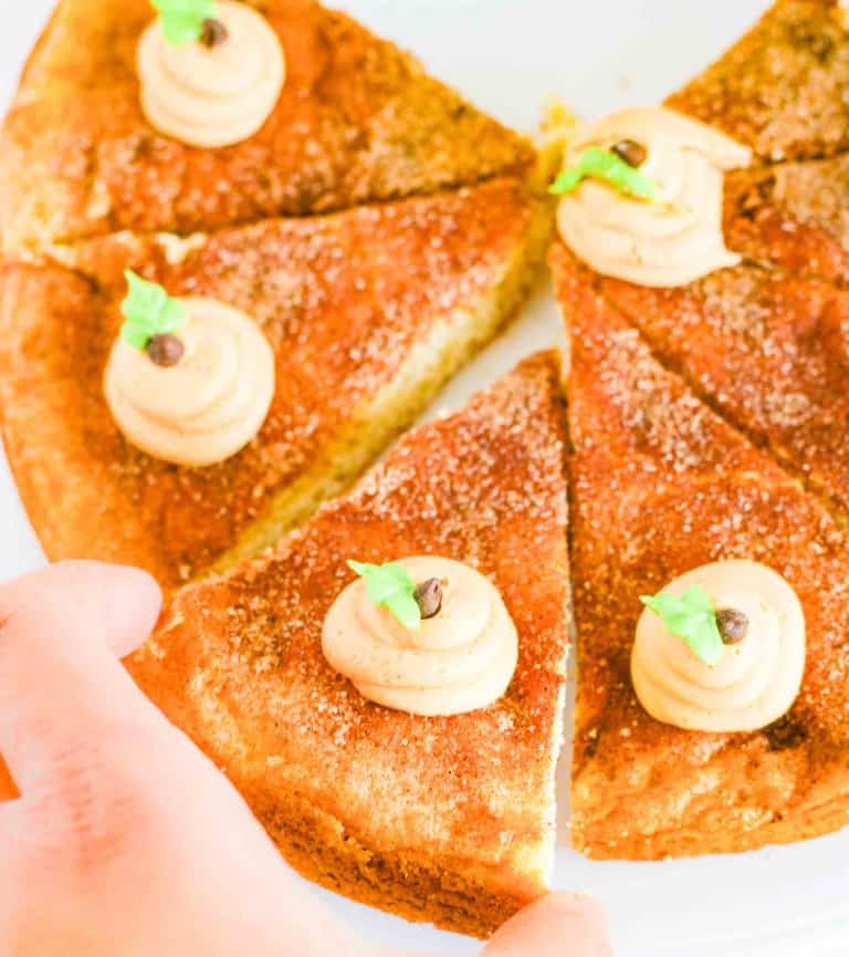 Five triangular slices of bread topped with swirls of spread, garnished with a small green leaf and a dark round topping; reminiscent of the inviting presentation you’d find with a snickerdoodle cookie cake, a hand is picking up one slice.