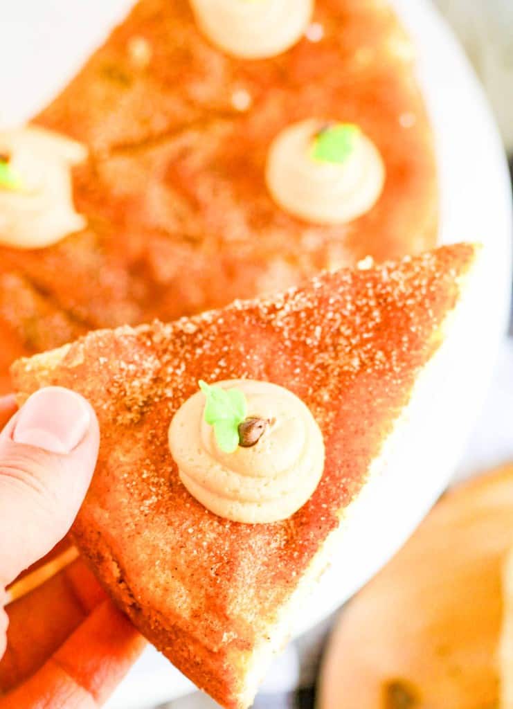 A hand holds a triangular slice of bread topped with a swirl of brown spread and a small green garnish, reminiscent of the cozy flavors found in a snickerdoodle cookie cake. More slices are on a white plate in the background.