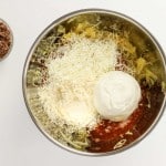A metal bowl with shredded cheese, ricotta, grated parmesan, tomato sauce, and shredded squash—perfect for preparing a delicious Spaghetti Squash Bake; ground beef and melted butter in small bowls nearby.