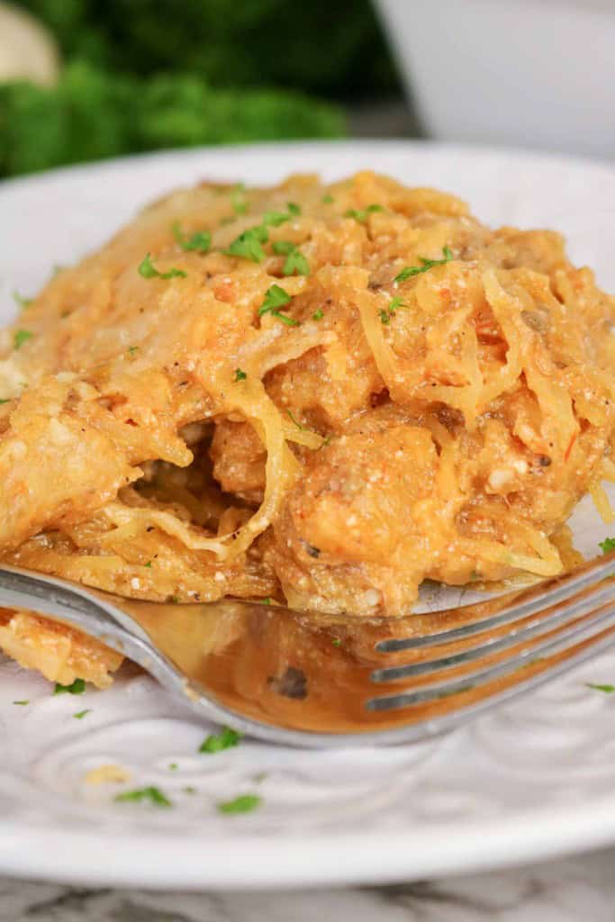 Close-up of a serving of Spaghetti Squash Bake on a white plate, garnished with chopped herbs, with a fork in the foreground.