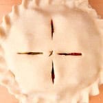 Unbaked strawberry rhubarb pie with crimped edges and four slits cut in the top crust, on a wooden surface.