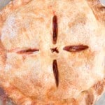 Golden brown strawberry rhubarb pie with four vents cut into the top crust, arranged in a cross pattern, resting on a light-colored surface.