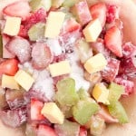 Unbaked strawberry rhubarb pie crust filled with chopped fruit, then topped with sugar and cubes of butter for a classic, tangy-sweet treat.