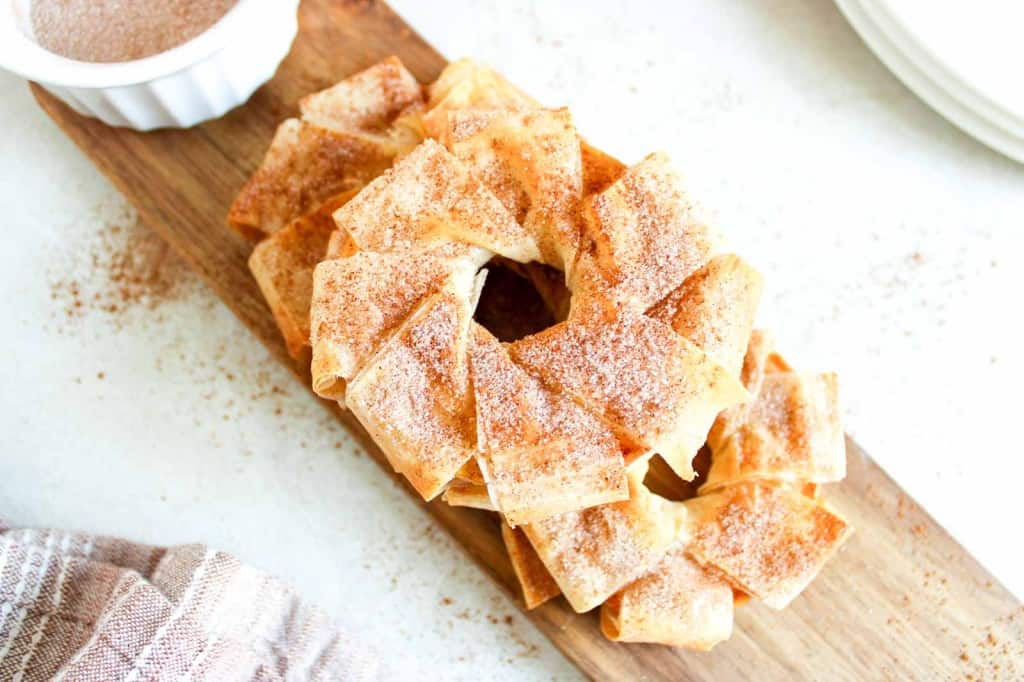 A stack of cinnamon sugar-coated tortilla chips arranged in a ring shape on a wooden serving board.