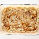 A glass baking dish lined with parchment paper, filled with swirled batter and chunks of apple, ready to be baked.
